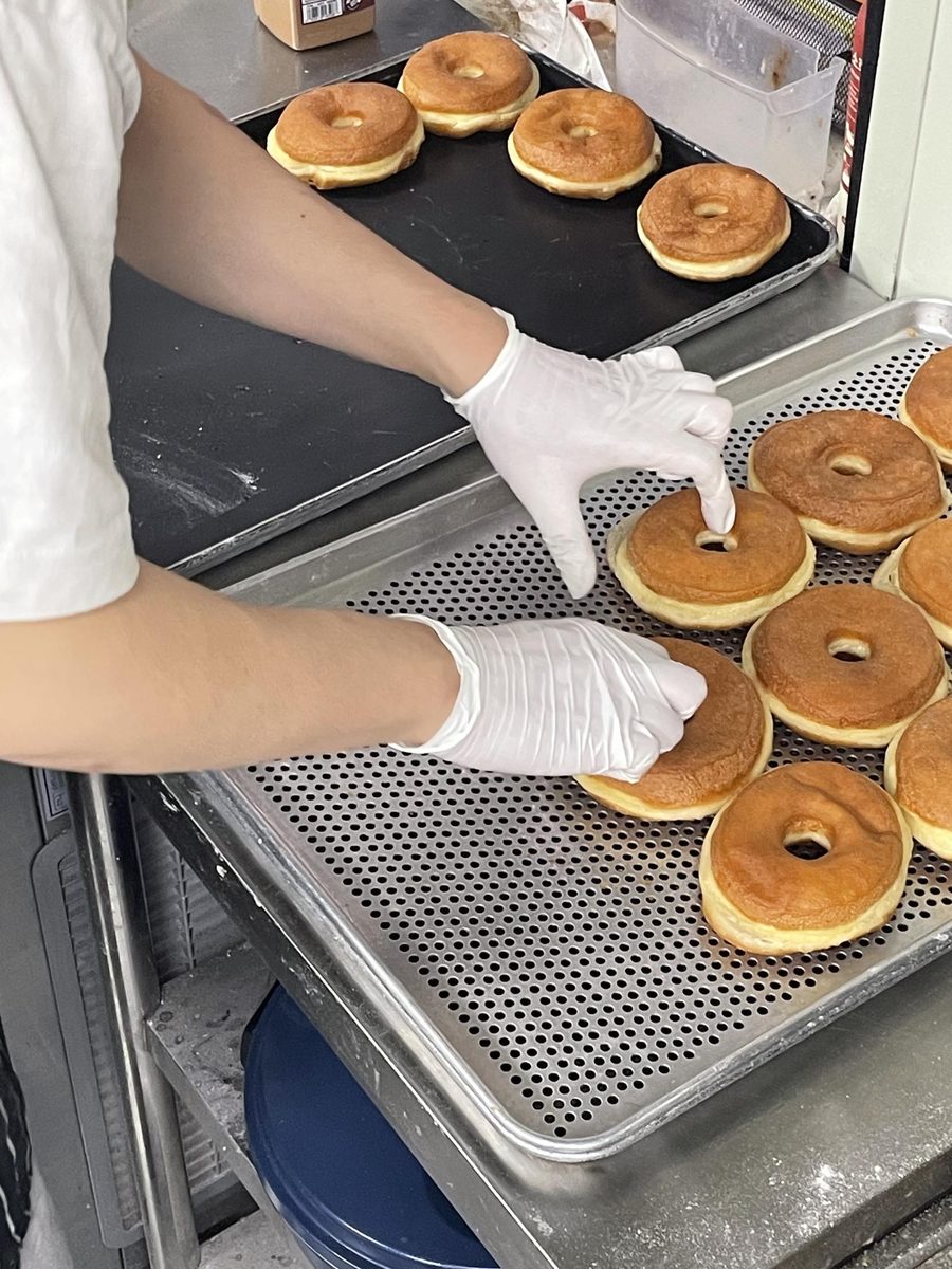 A gloved hand checking a fried donut on a perforated cooling tray