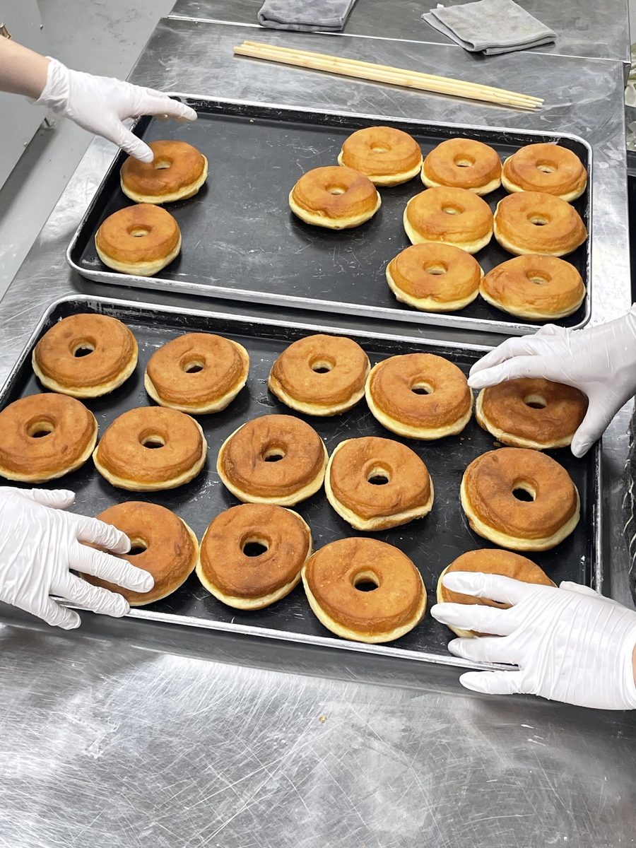 Freshly fried donuts being lined up on trays by gloved hands